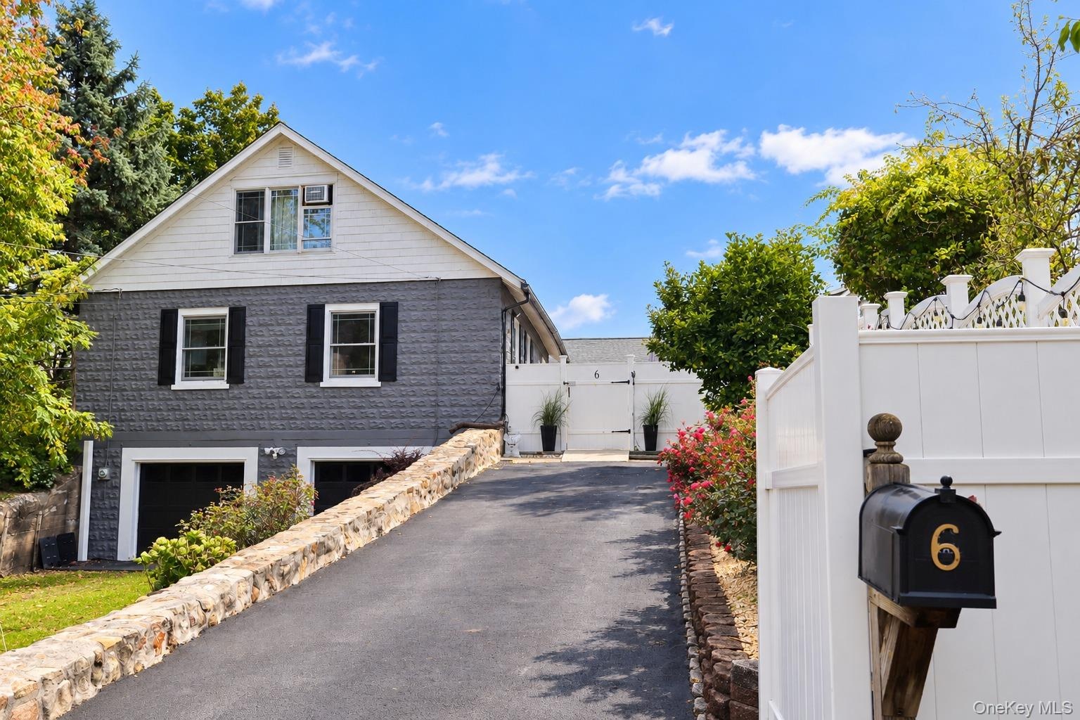 Exterior featuring a two-tone stone and siding facade, an asphalt driveway lined with stone retaining walls, and a white privacy gate