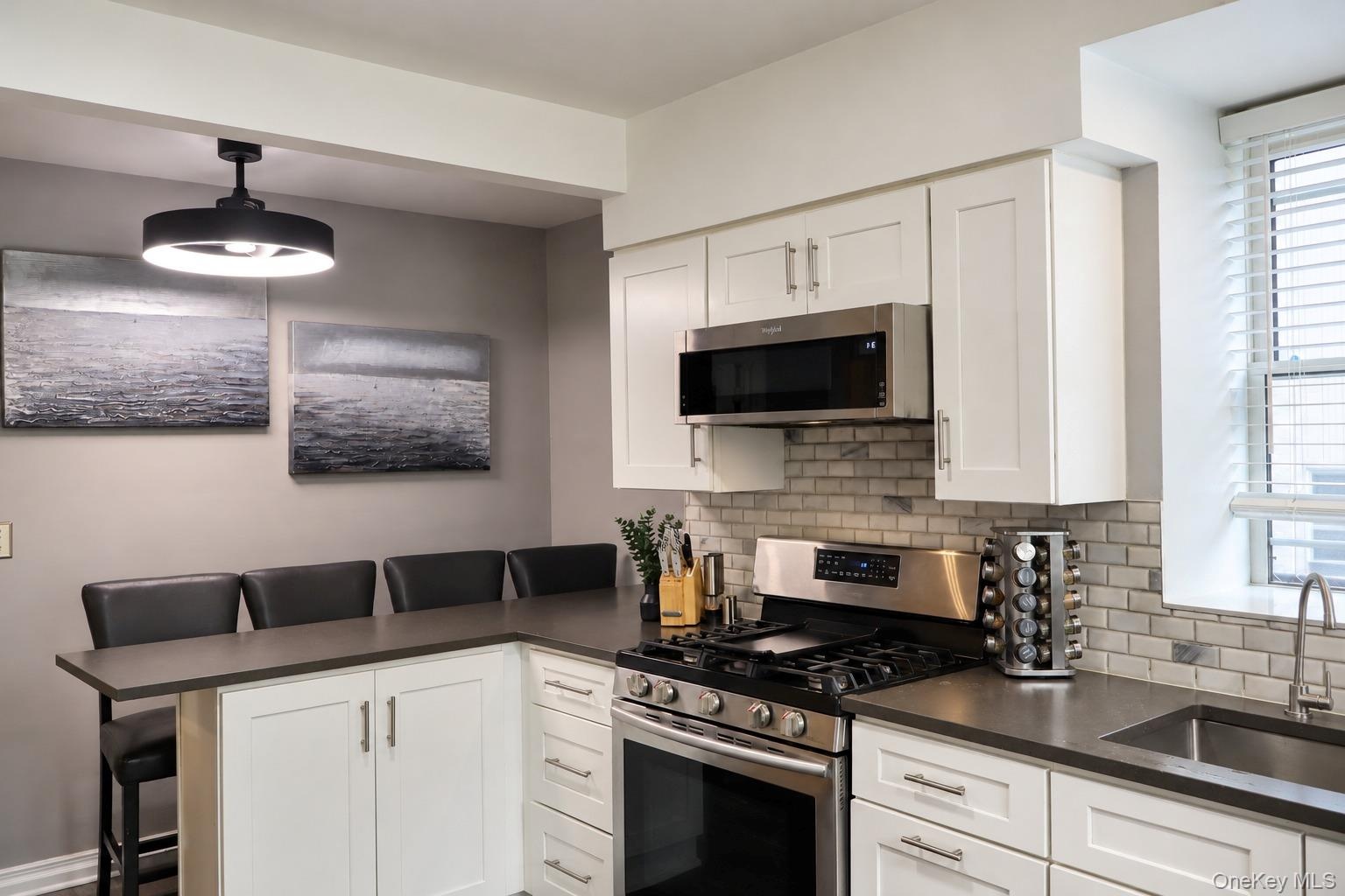 Kitchen featuring white Shaker-style cabinetry, dark solid-surface countertops, stainless steel appliances, subway tile backsplash, and a contemporary