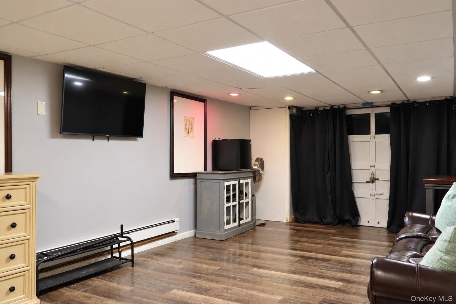 Finished space featuring wood-finish flooring, drop ceiling with recessed lighting, and wall-mounted television bracket