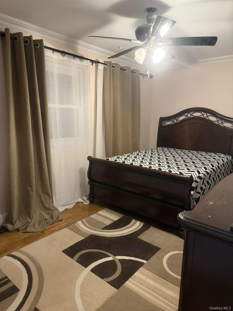 Room featuring wood-finish flooring, crown molding, and a multi-blade ceiling fan with integrated lighting