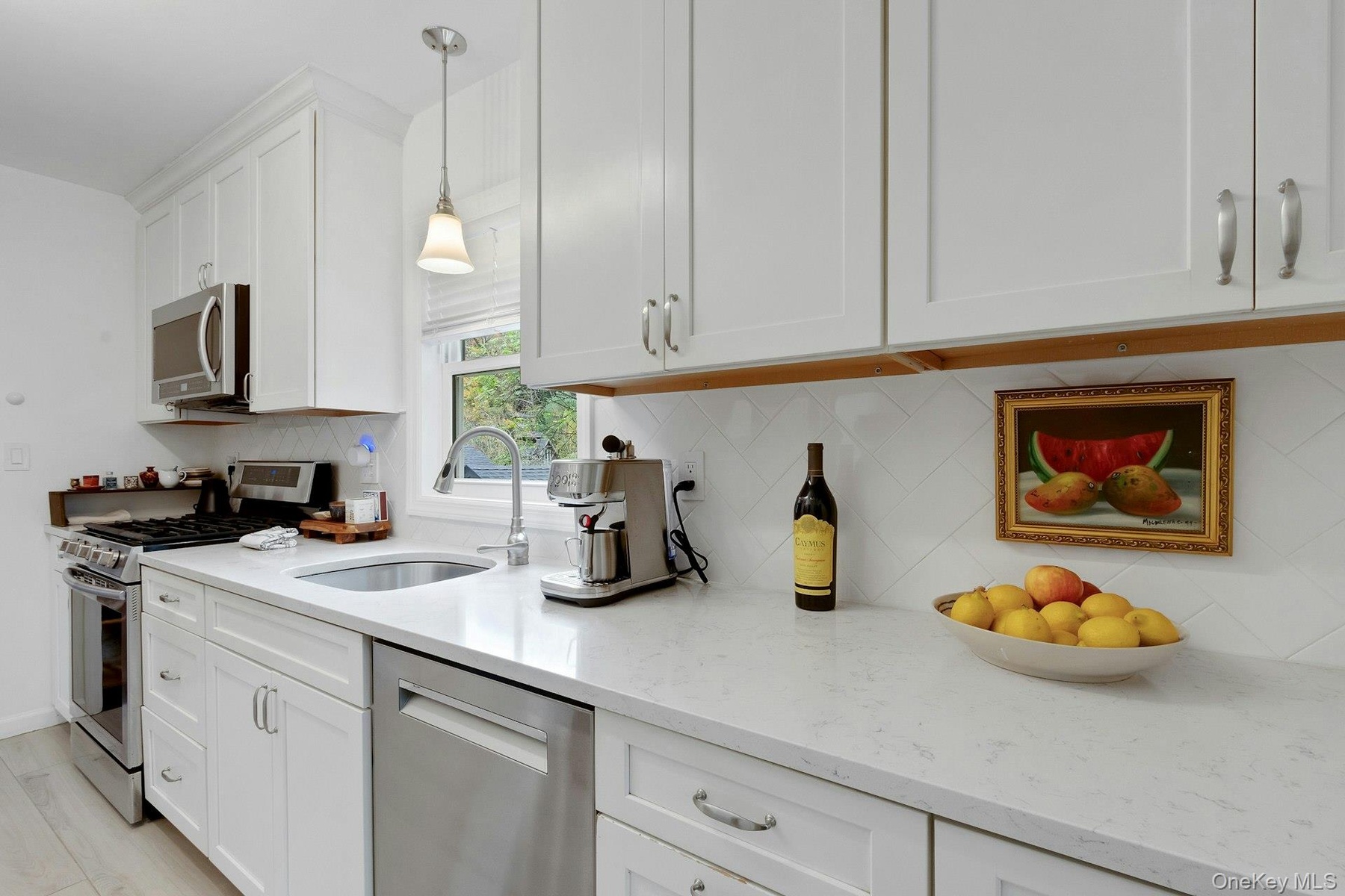 Kitchen with appliances with stainless steel finishes, pendant lighting, light stone counters, white cabinets