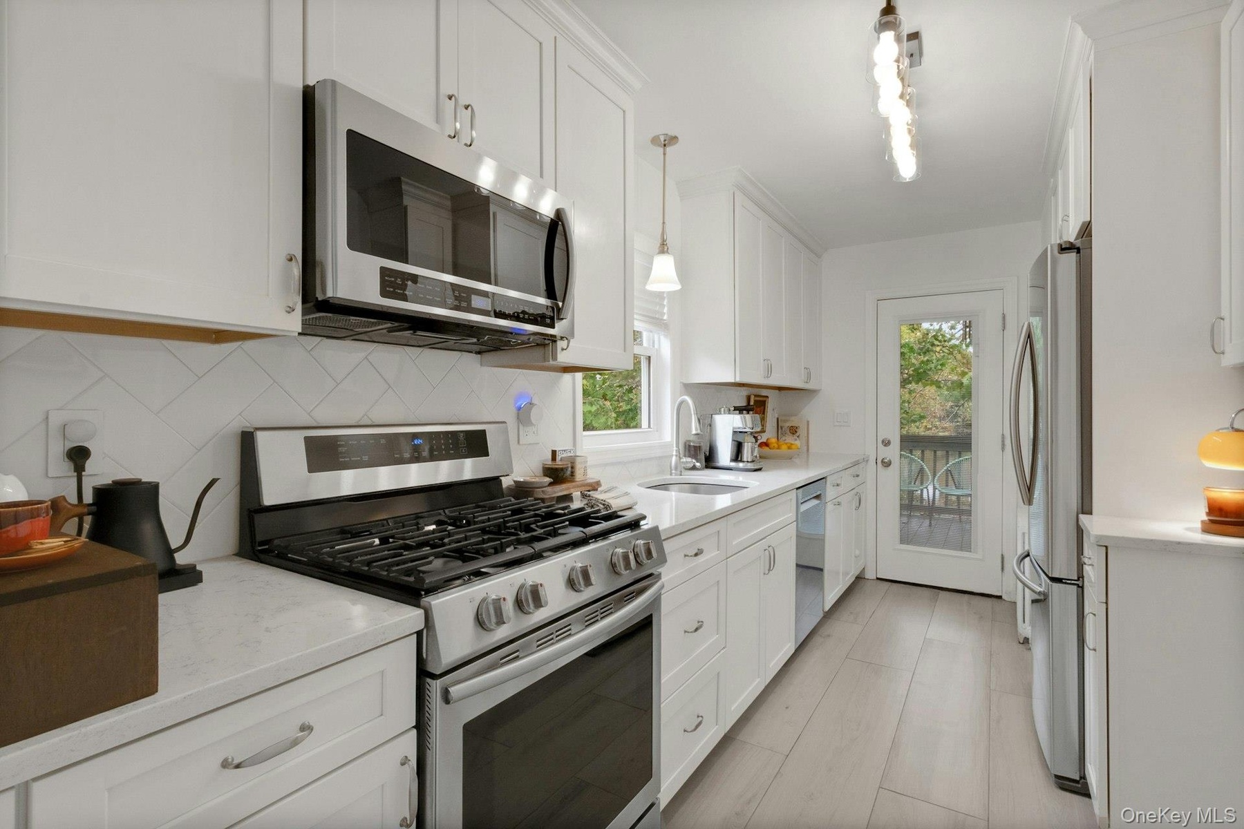 Kitchen with appliances with stainless steel finishes, pendant lighting, light stone counters, white cabinets, and light wood-style floor