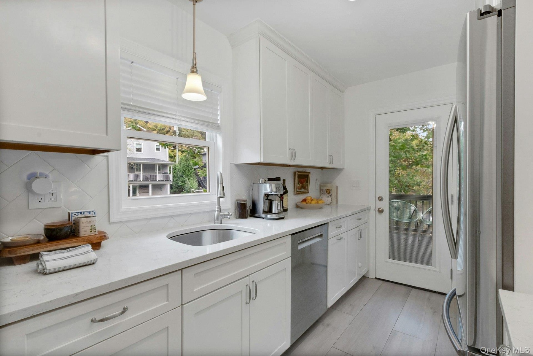 Kitchen with appliances with stainless steel finishes, pendant lighting, light stone counters, white cabinets