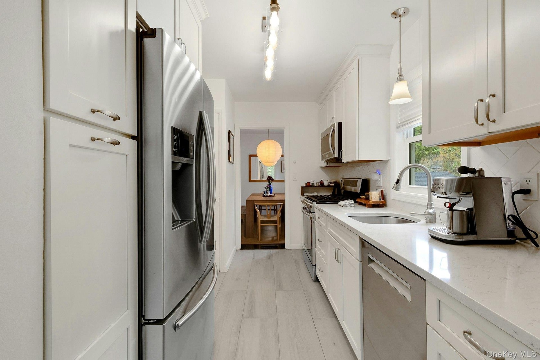 Kitchen with appliances with stainless steel finishes, pendant lighting, light stone counters, white cabinets