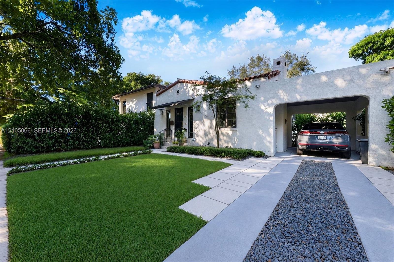 Stucco exterior featuring a tiled roof, arched carport, paved driveway with gravel center inlay, and manicured front lawn