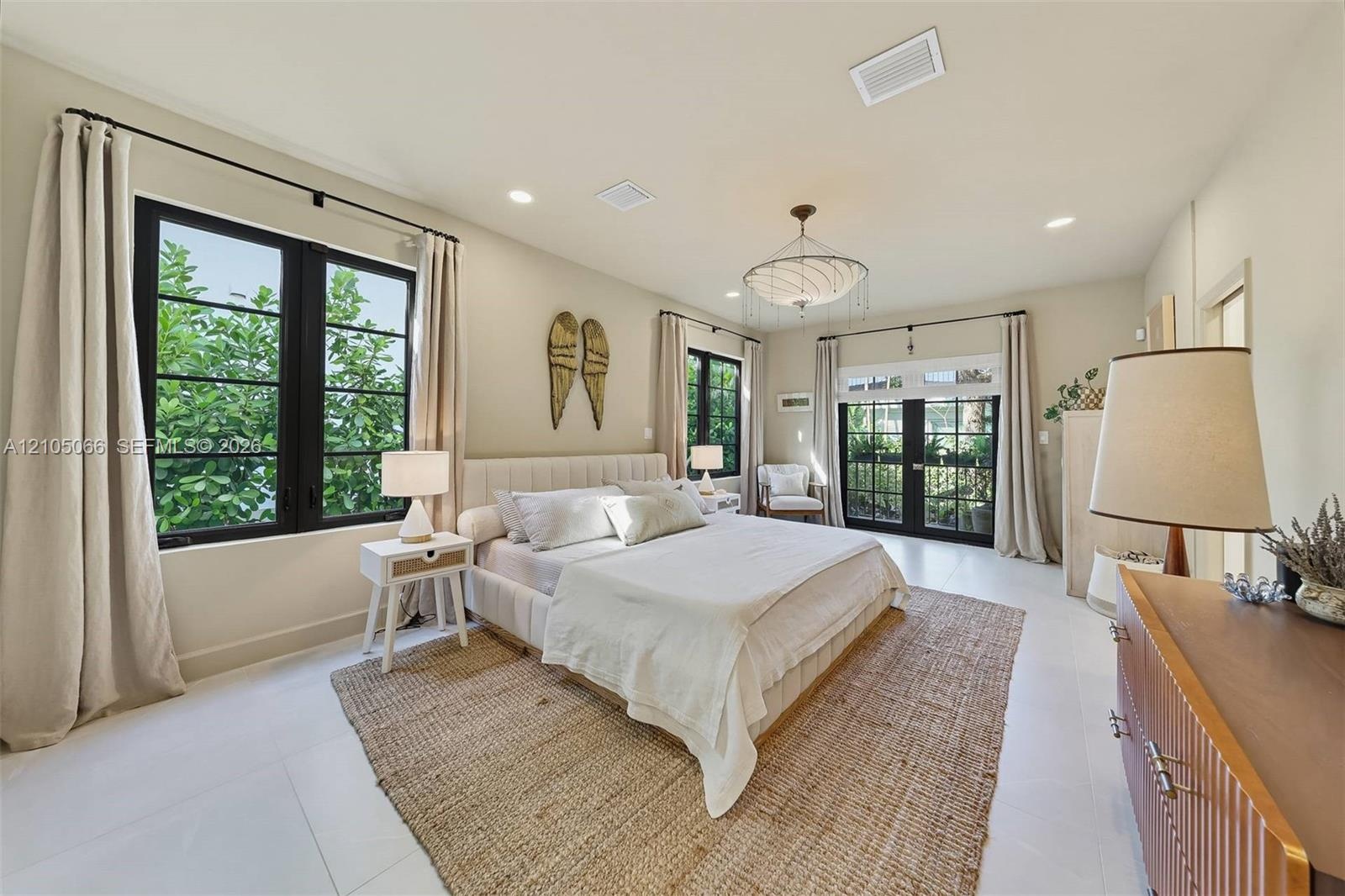 Neutral interior featuring large-format tile flooring, recessed lighting, a modern multi-tiered chandelier, black-framed windows, and a set of glass-p