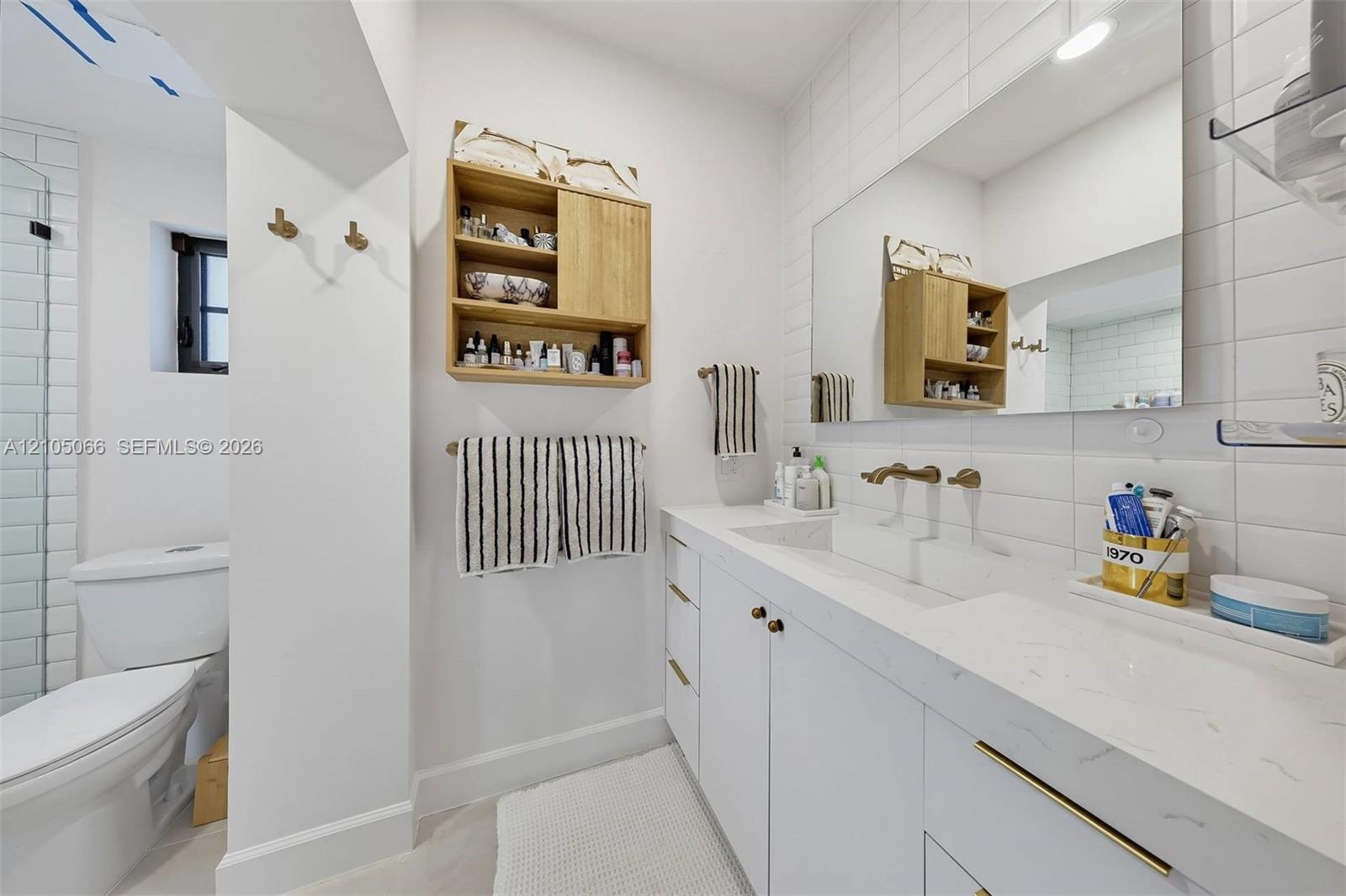Bathroom featuring a white vanity with integrated double sinks, quartz countertop, brass-tone hardware, wall-mounted faucets, and subway tile wall sur