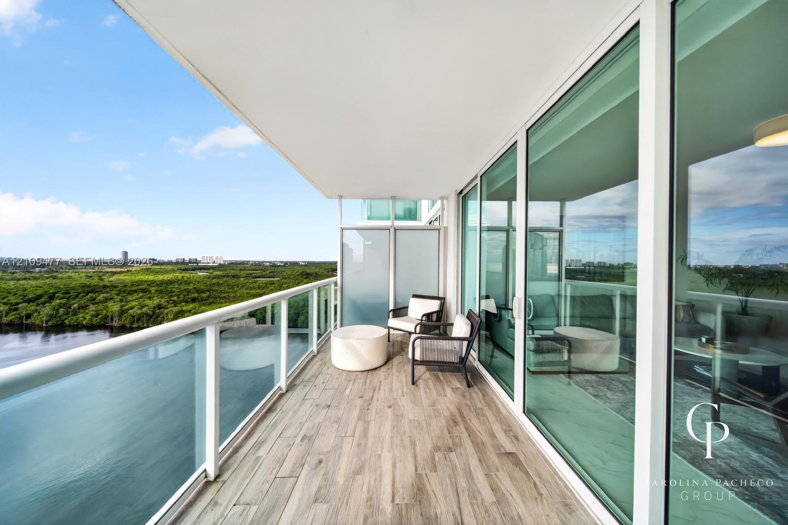 Covered balcony with wood-finish flooring, glass panel railings, and floor-to-ceiling sliding glass doors