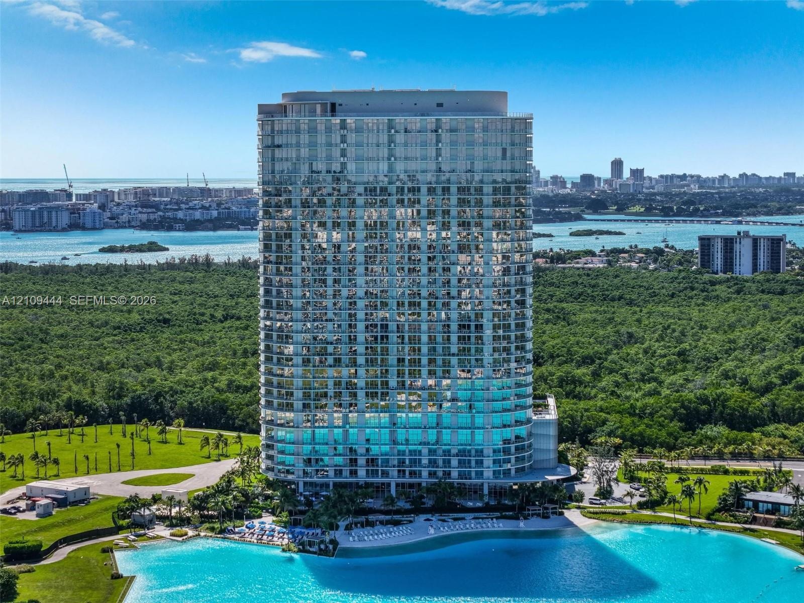 High-rise residential tower featuring a glass-curtain wall exterior, private balconies, and a multi-level structure positioned on a waterfront site wi
