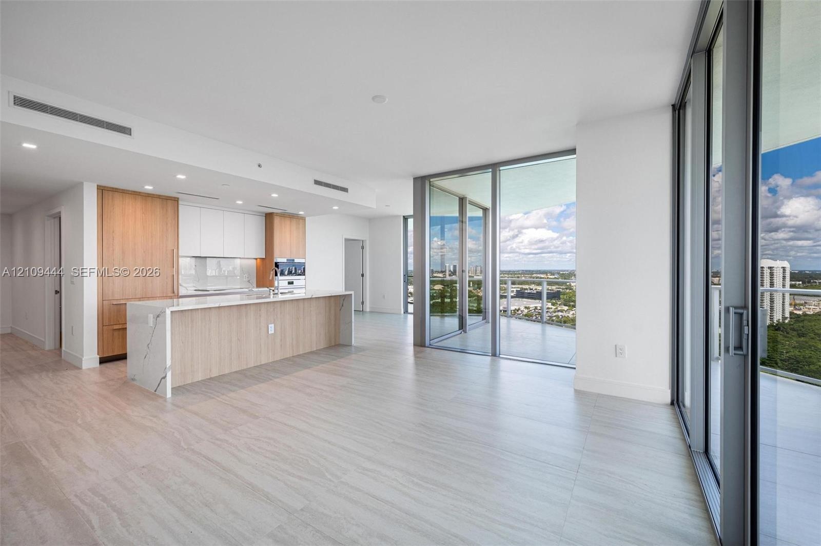 Open-concept kitchen featuring wood-finish cabinetry, a waterfall-edge stone island, built-in stainless steel appliances, wood-finish flooring, and fl