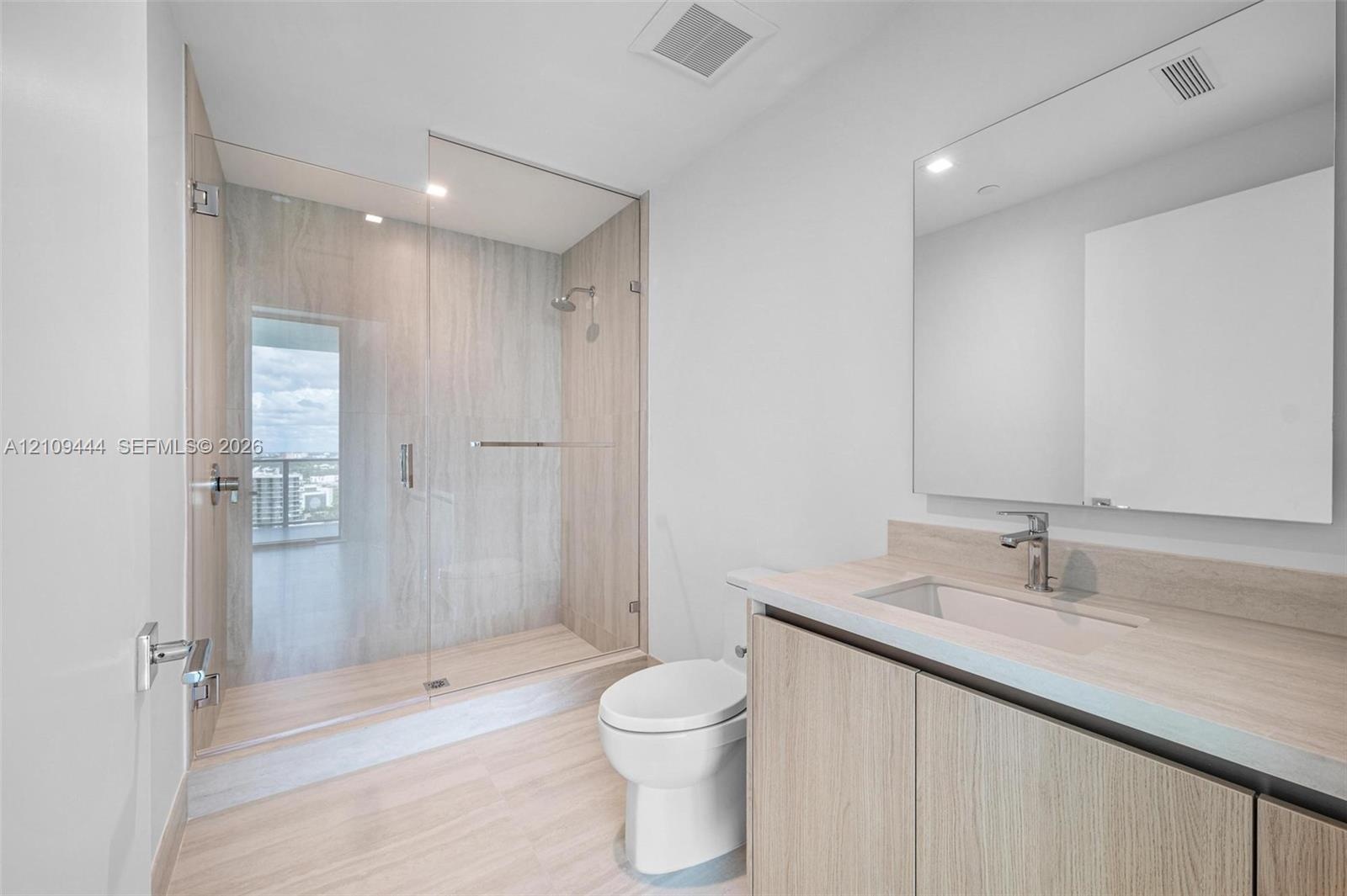 Bathroom featuring wood-finish cabinetry, a large integrated mirror, a walk-in shower with a glass enclosure and floor-to-ceiling wall tile, and light