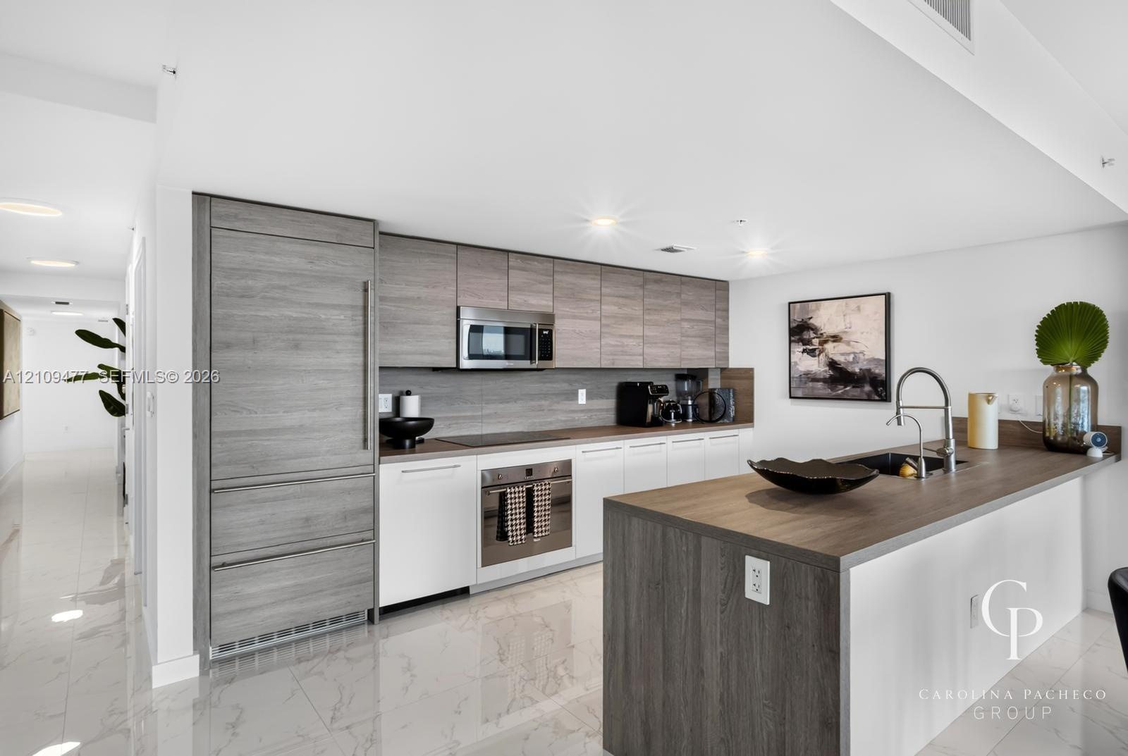 Contemporary kitchen featuring wood-finish cabinetry, a waterfall-edge kitchen island, integrated refrigerator, stainless steel appliances, and polish