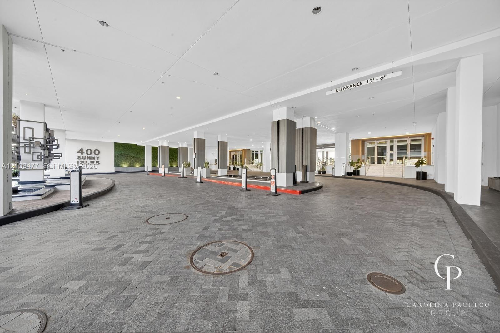 Covered porte-cochère featuring a herringbone-patterned stone driveway, recessed lighting, integrated vertical accent columns, and a decorative living
