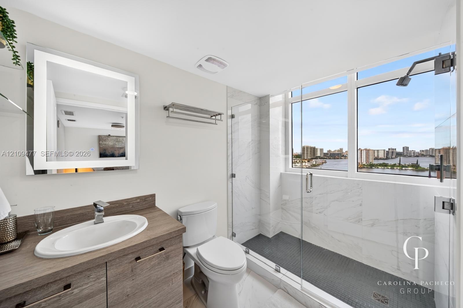 Bathroom featuring a wood-finish vanity with an integrated basin, a backlit mirror, and a walk-in shower with stone-tile surround, dark floor tiling, 