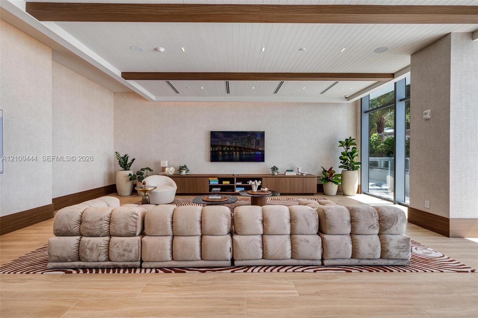 Living area featuring wood-finish flooring, planked ceiling with recessed wood beams, built-in media cabinetry, and floor-to-ceiling windows