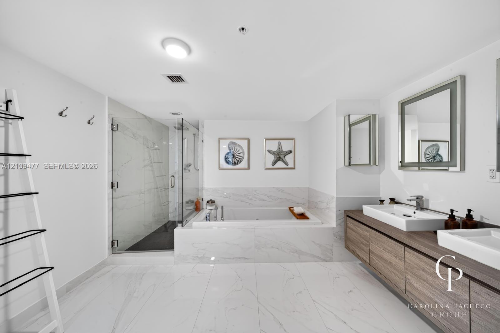 Bathroom featuring a wall-mounted double vanity with wood-finish cabinetry, rectangular vessel sinks, large-format tile flooring, a glass-enclosed wal