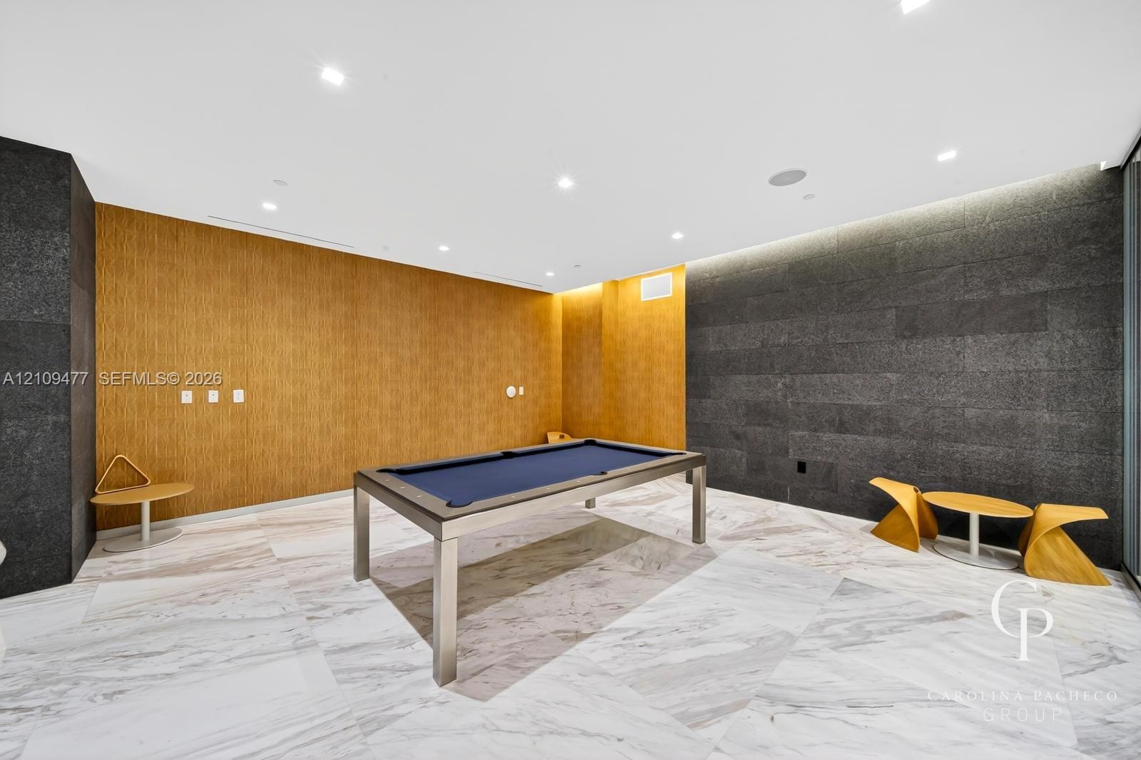 Interior space featuring large-format stone floor tiles, natural wood-finish wall paneling, charcoal-toned stone feature walls, and recessed ceiling l