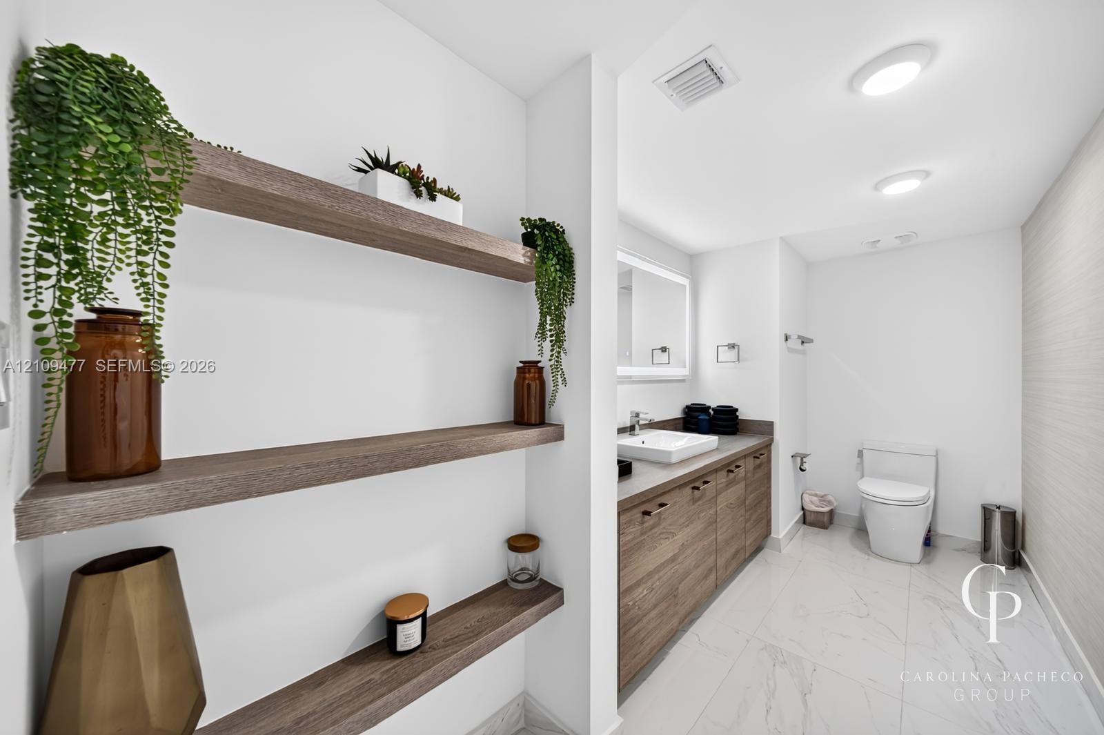 Bathroom featuring wood-finish floating shelving, wood-grain vanity cabinetry, square vessel sink, and large-format stone-tile flooring