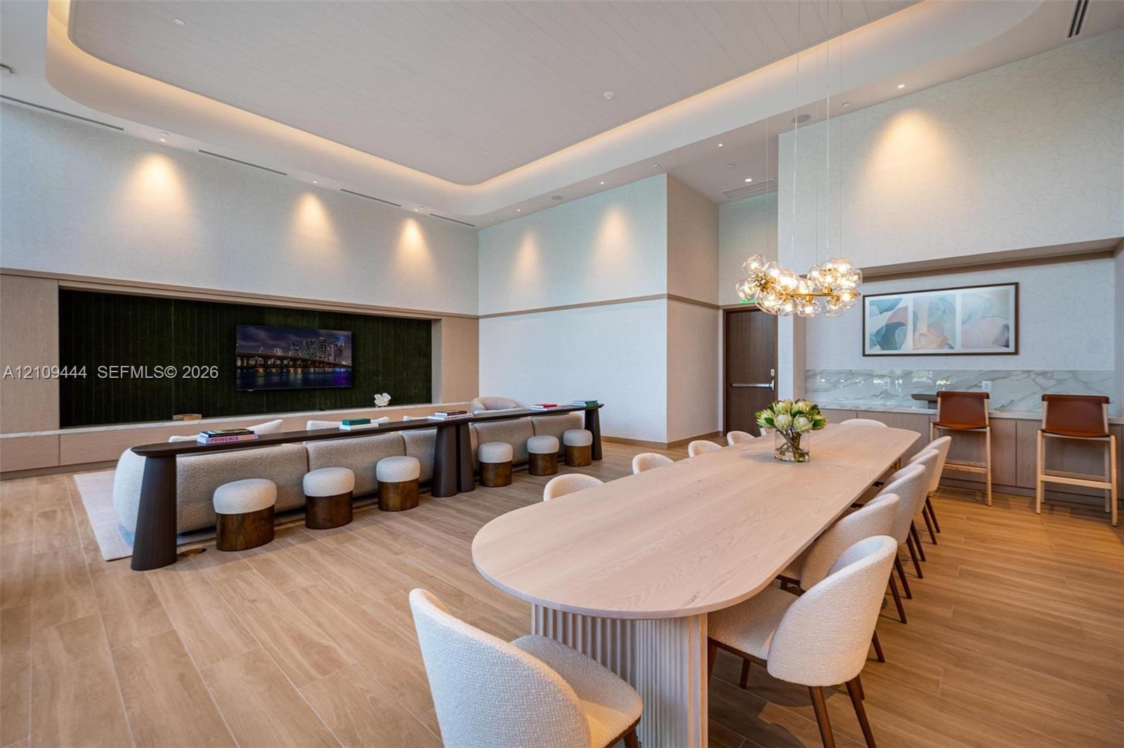 High-ceiling interior featuring recessed tray lighting, wood-finish flooring, a built-in entertainment niche, and a custom bar area with stone-finish 