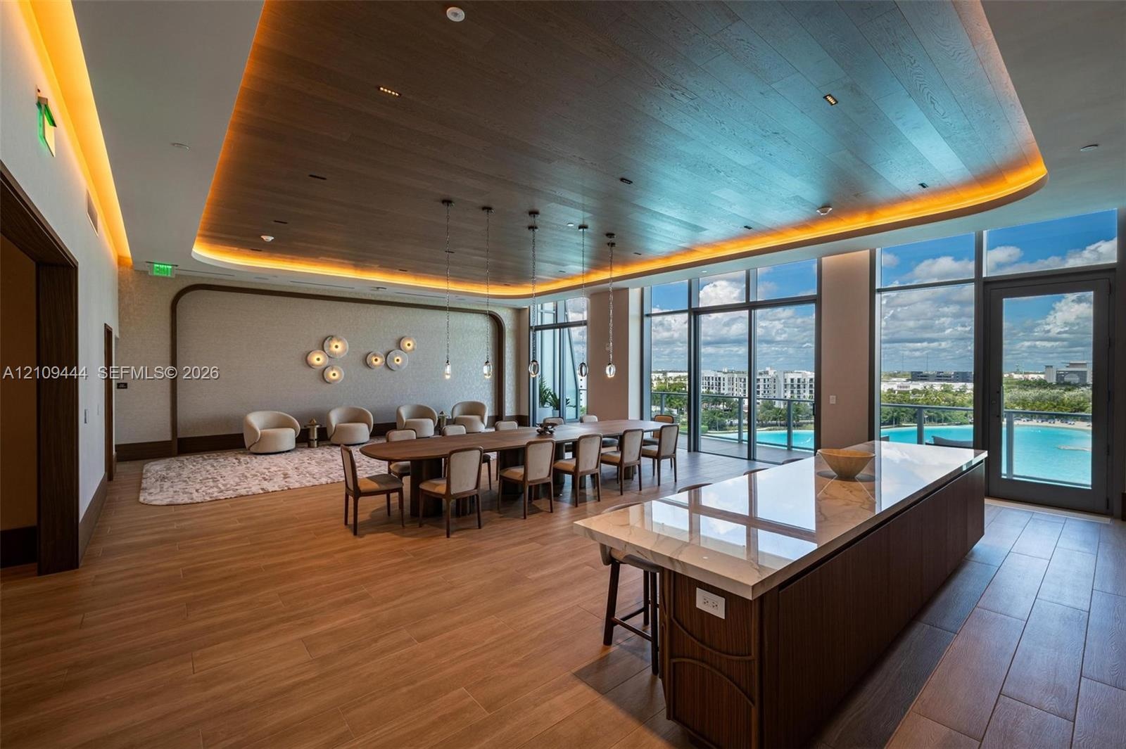 Expansive interior featuring a wood-paneled tray ceiling with recessed ambient lighting, floor-to-ceiling windows, wood-finish flooring, and a large k