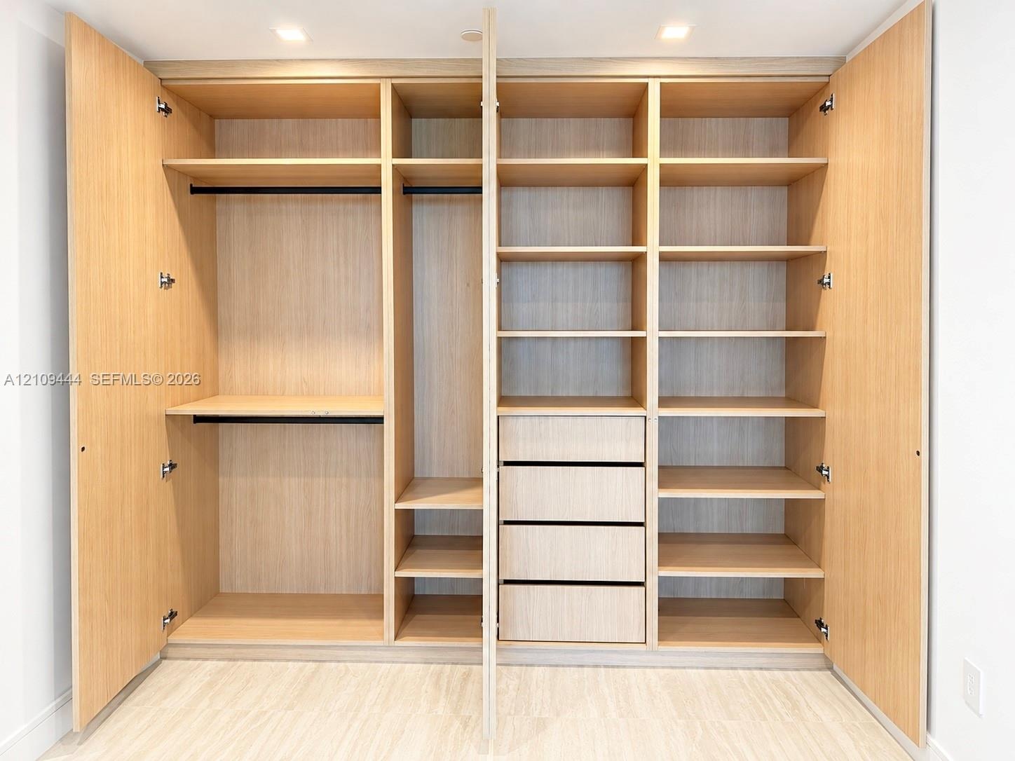 Custom floor-to-ceiling cabinetry with light wood finish, integrated hanging rods, multiple adjustable shelving tiers, and built-in drawer storage