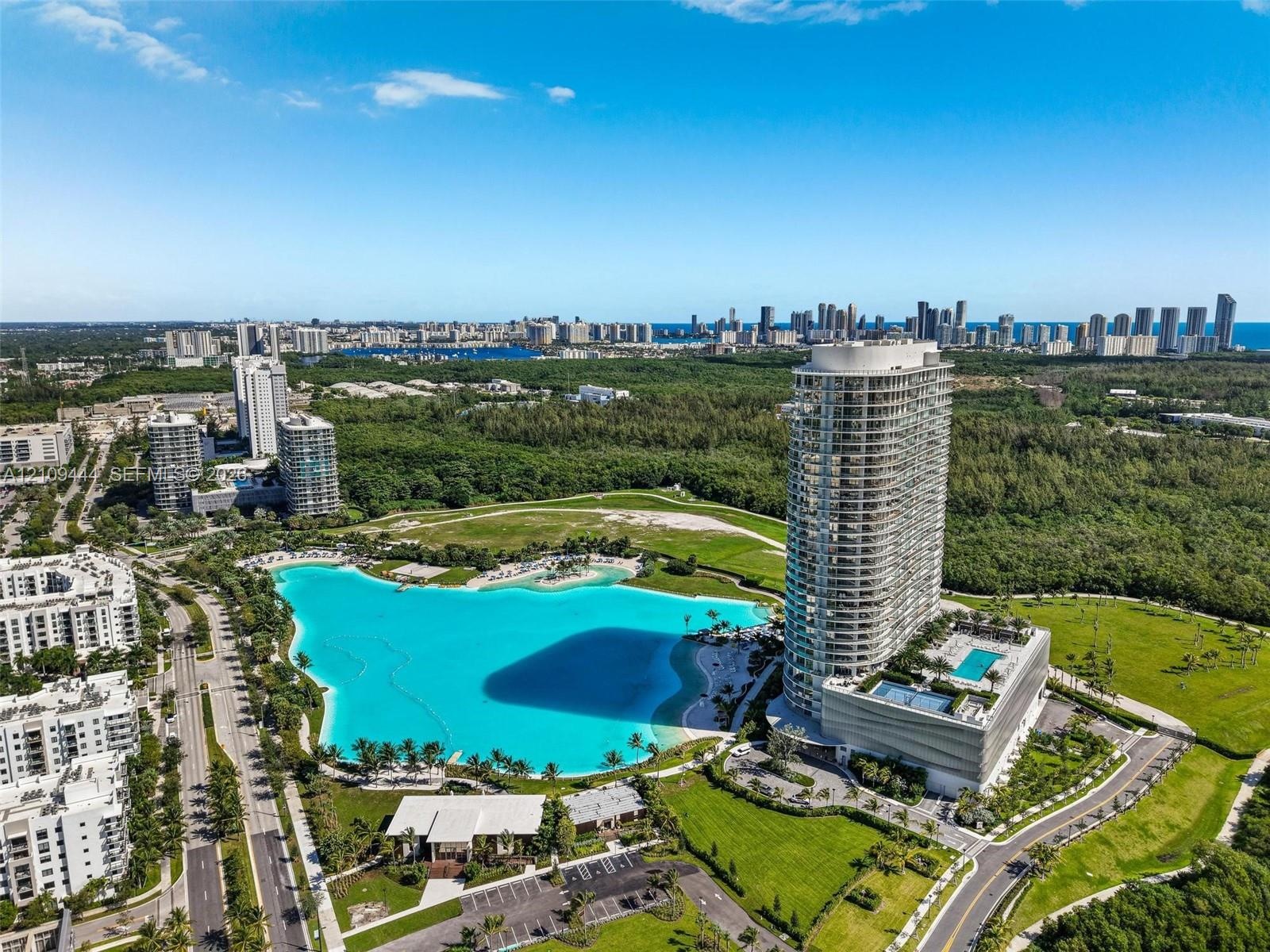 Aerial perspective of a high-rise residential tower featuring a multi-level podium, an attached swimming pool, landscaped grounds, and a central lagoo