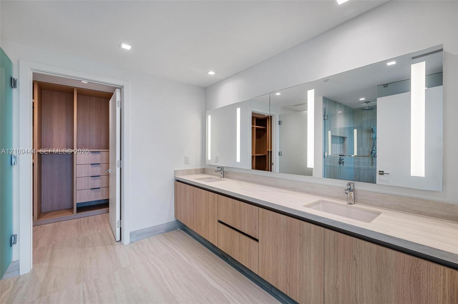 Floating double vanity with wood-finish cabinetry, integrated rectangular sinks, expansive wall-to-wall mirror with built-in vertical lighting, and la
