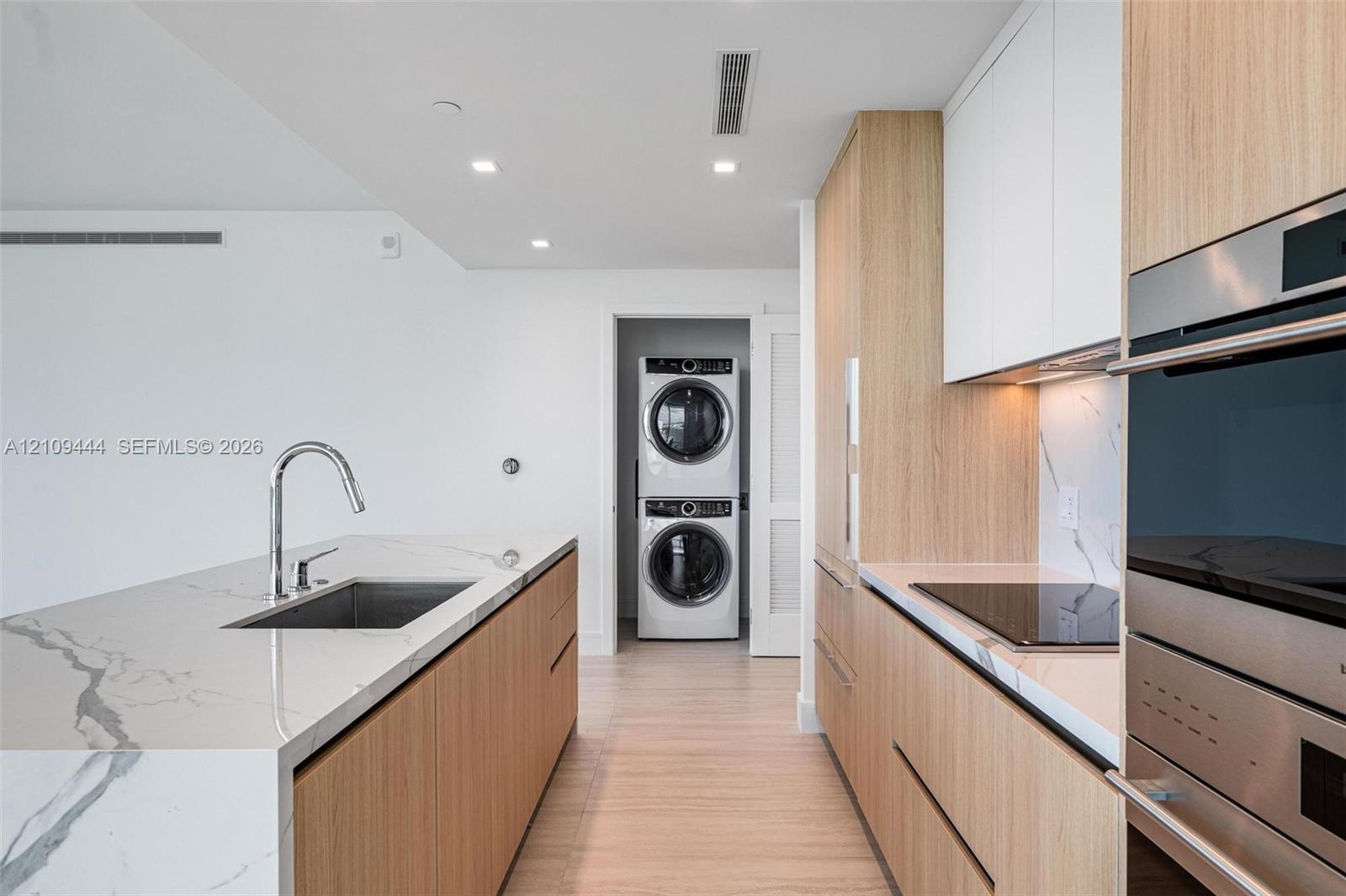 Kitchen featuring wood-finish cabinetry, stone-surface countertops, stainless steel undermount sink with gooseneck faucet, built-in wall oven, and sta