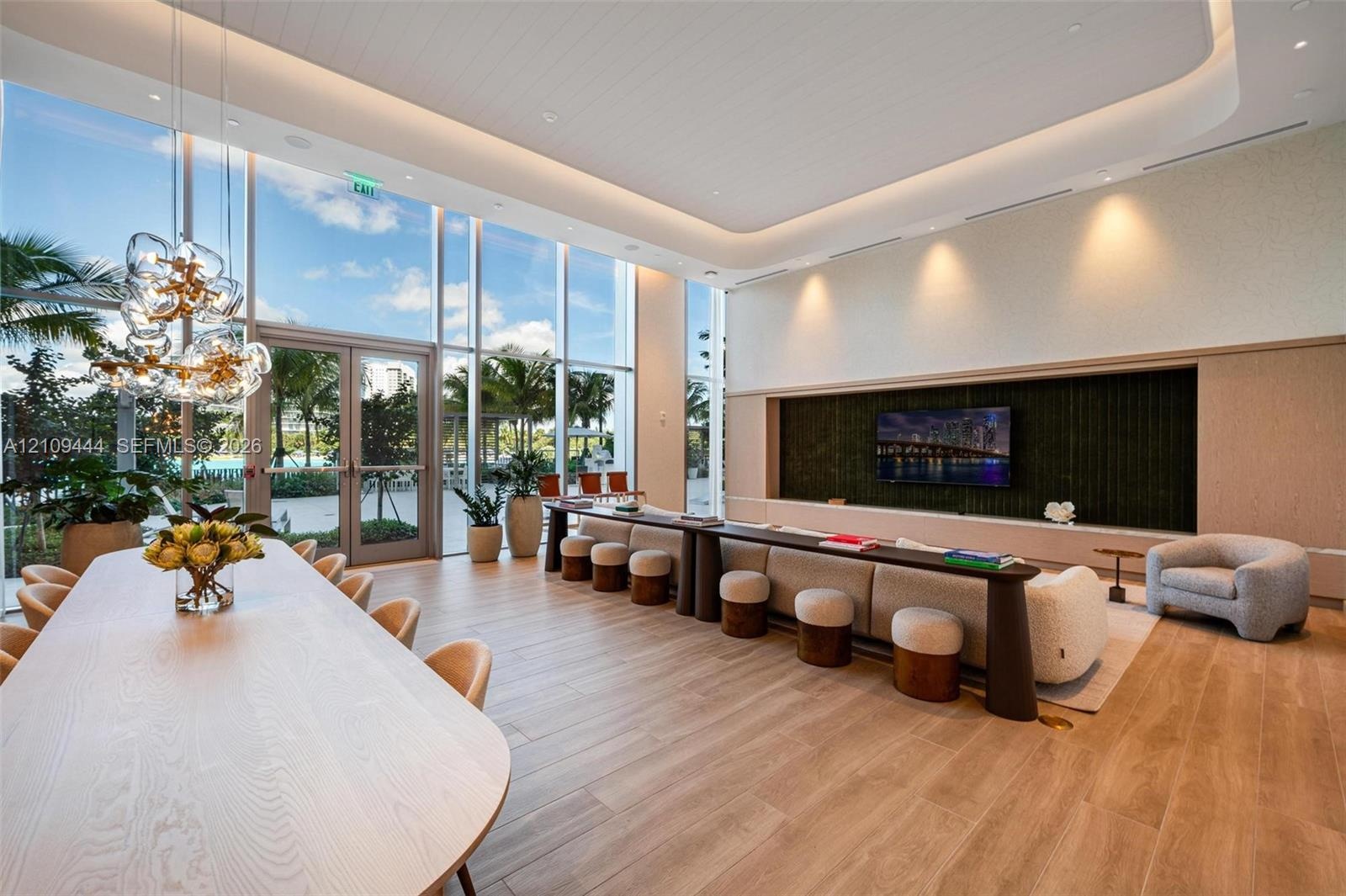 Floor-to-ceiling glass walls, wood-finish flooring, recessed tray ceiling with cove lighting, custom built-in media console, and statement multi-penda