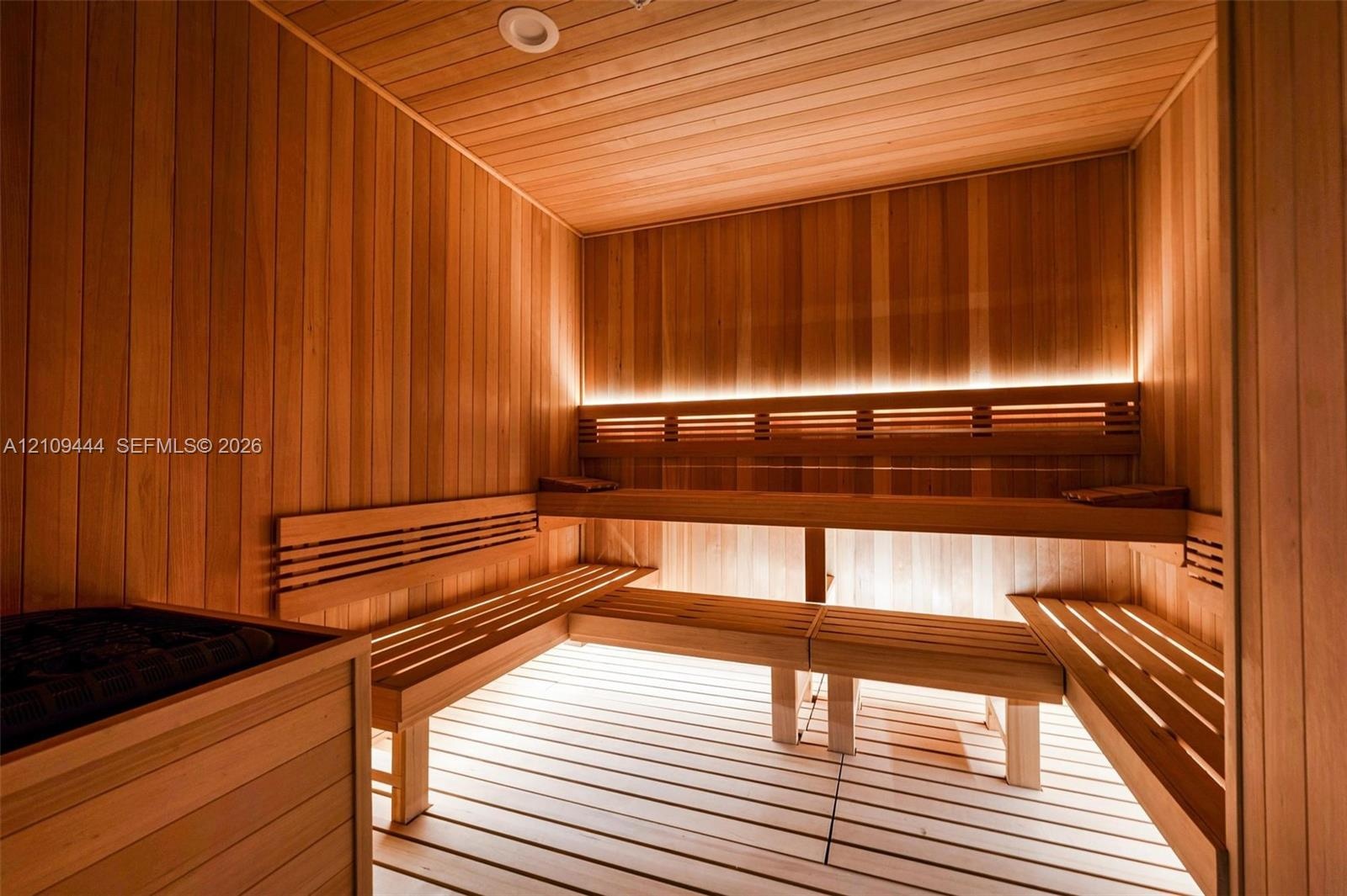Sauna featuring wood-plank wall paneling, multi-level slatted wood benches, hidden LED accent lighting, and a built-in heating unit