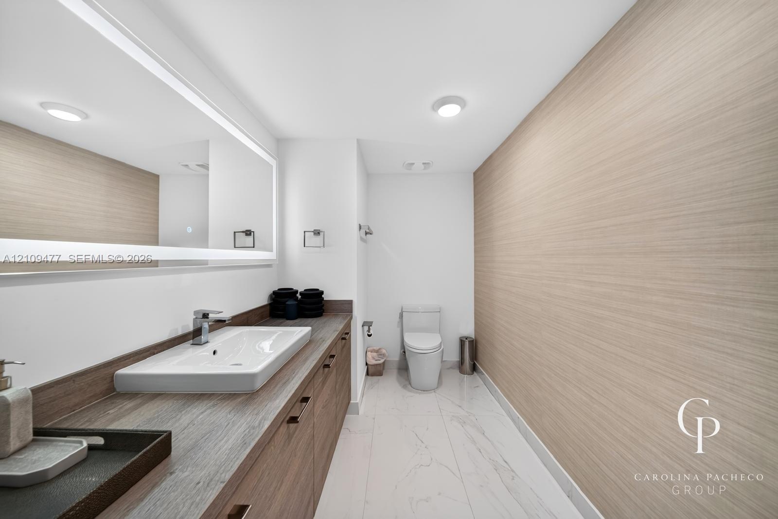 Bathroom featuring a wood-finish vanity with a rectangular vessel sink, integrated lighting mirror, stone-finish countertop, and large-format tile flo