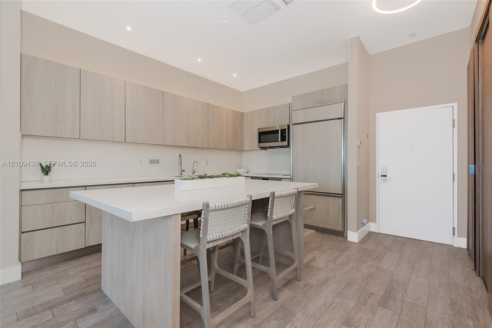 Kitchen featuring wood-finish cabinetry, stone-surface center island, stainless steel built-in appliances, and wood-finish flooring