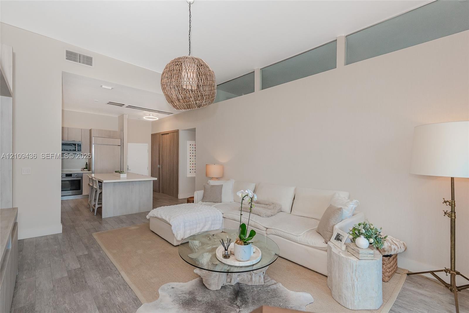 High-ceiling living area featuring clerestory windows, wood-finish flooring, a woven pendant light fixture, and an integrated kitchen with a stone-sur
