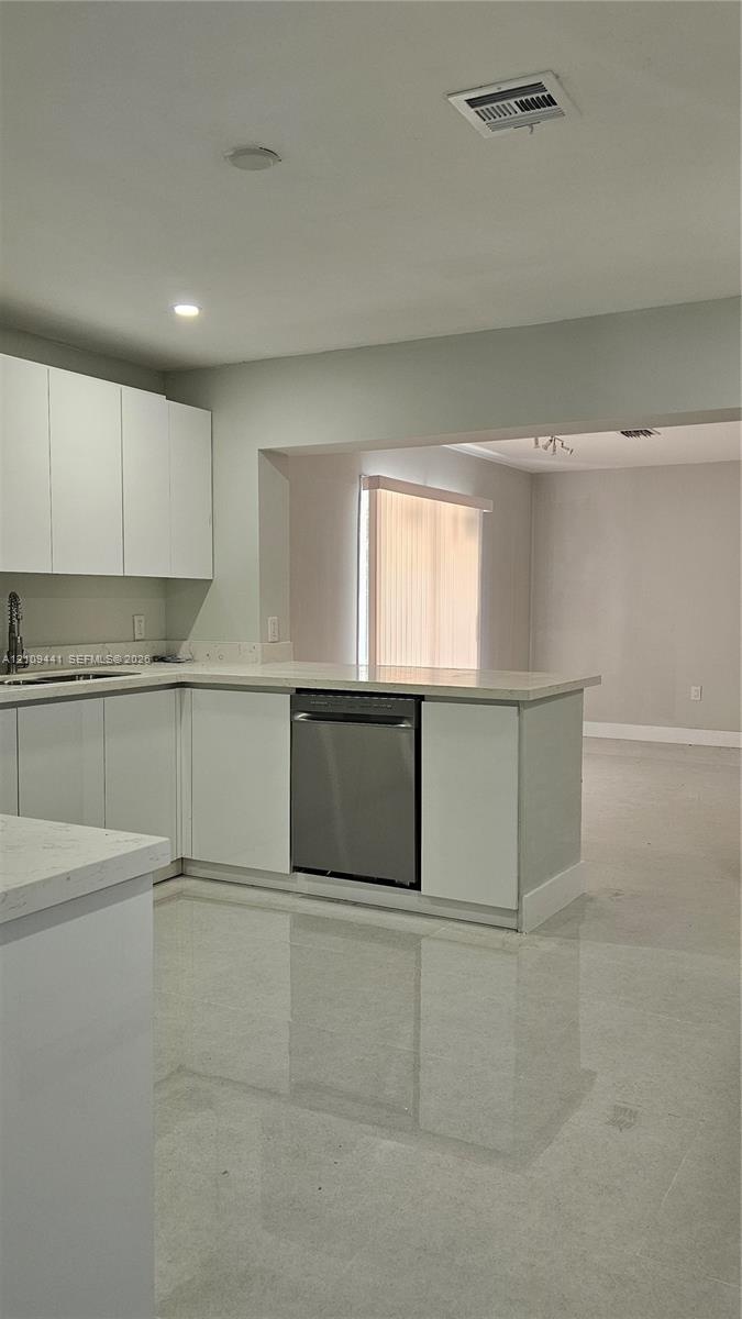 Kitchen featuring white flat-panel cabinetry, stone-style countertops, integrated stainless steel dishwasher, and polished light-toned flooring