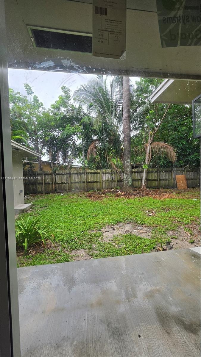 Backyard featuring a concrete patio, grass lawn, wood perimeter fencing, and mature trees