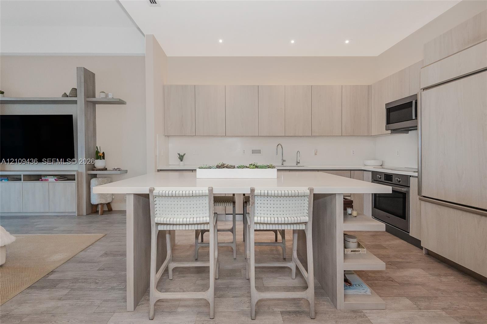 Modern kitchen featuring light wood-finish cabinetry, a large central island with a solid surface countertop, integrated stainless steel appliances, r