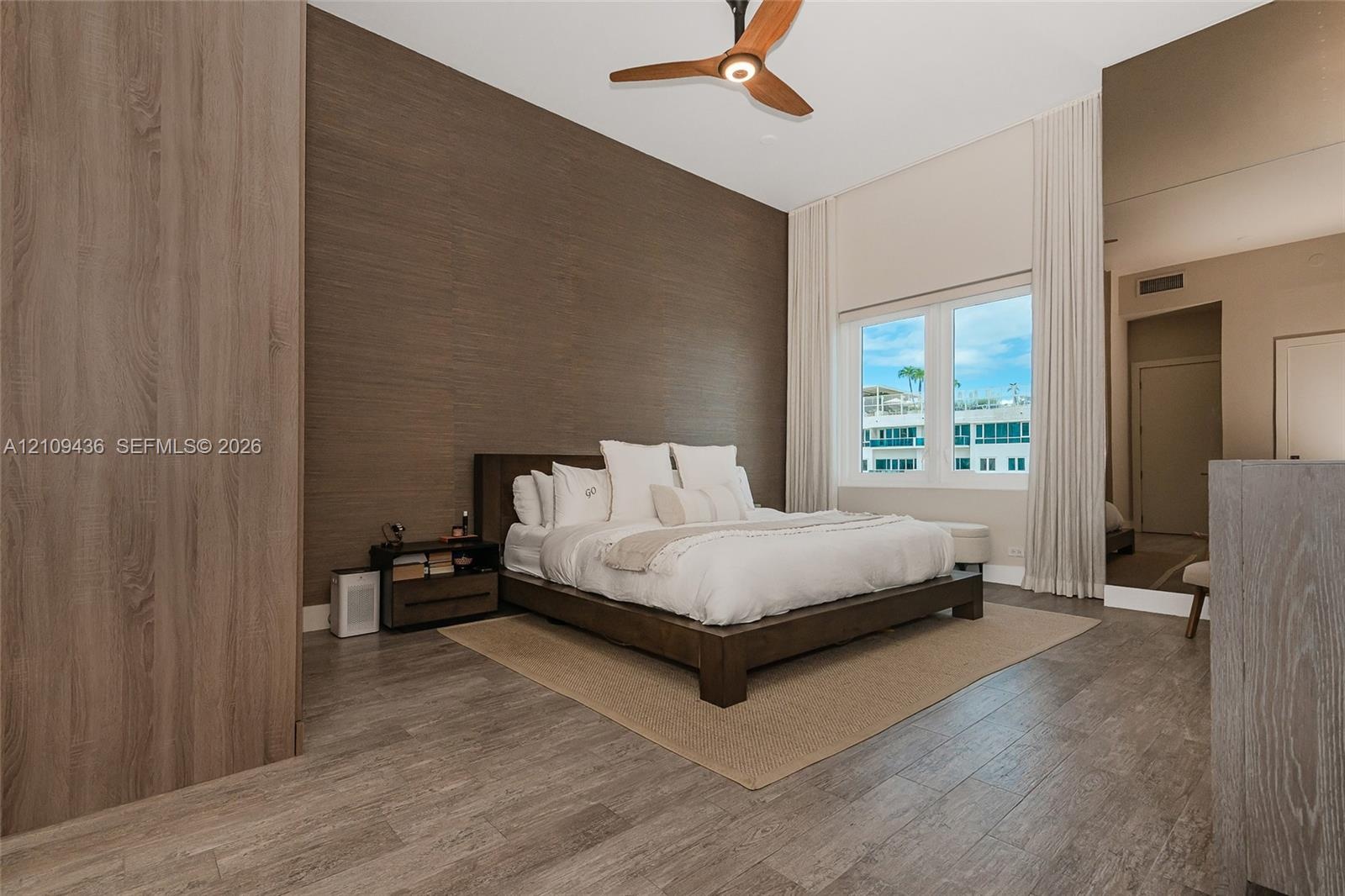 High-ceiling room featuring wood-finish flooring, a full-height decorative wood-paneled wall, a modern three-blade ceiling fan, and a floor-to-ceiling