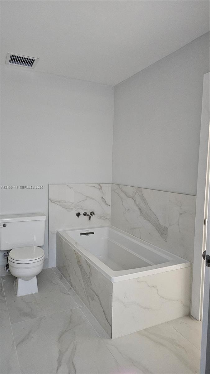 Bathroom featuring a deep soaking tub with a wall-mounted faucet, complemented by large-format tile flooring and matching tile surround