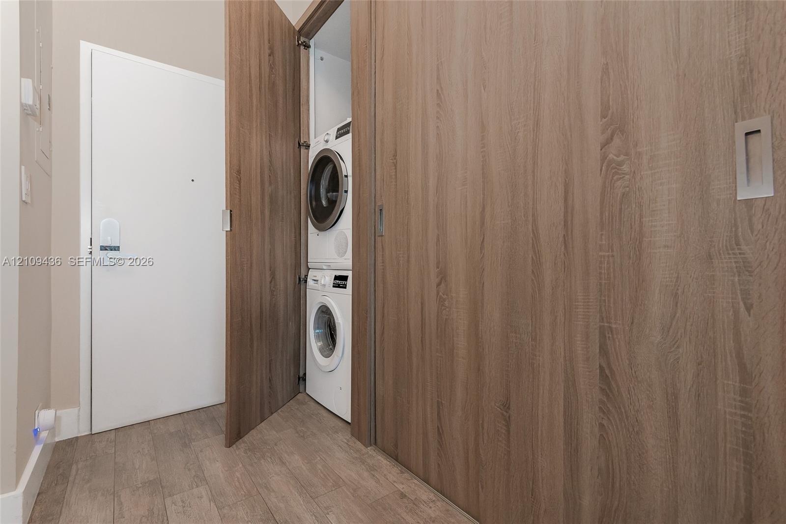 Laundry closet featuring a stackable washer and dryer unit, wood-finish cabinetry, and sliding door paneling