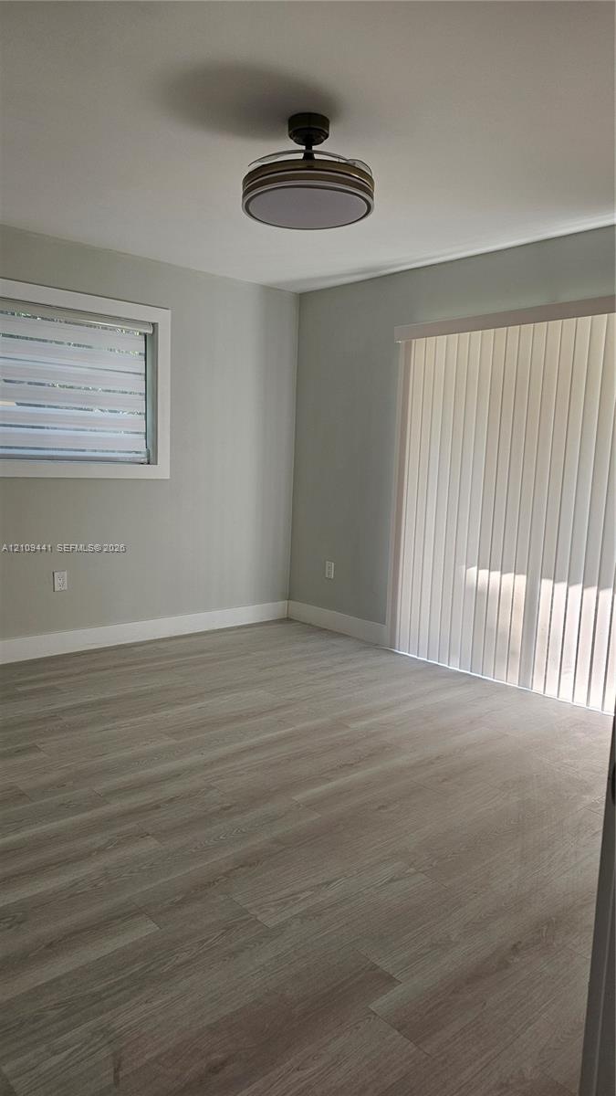 Neutral wall tones, wood-finish flooring, ceiling-mounted light fixture, sliding glass door with vertical blinds, and window with horizontal blinds