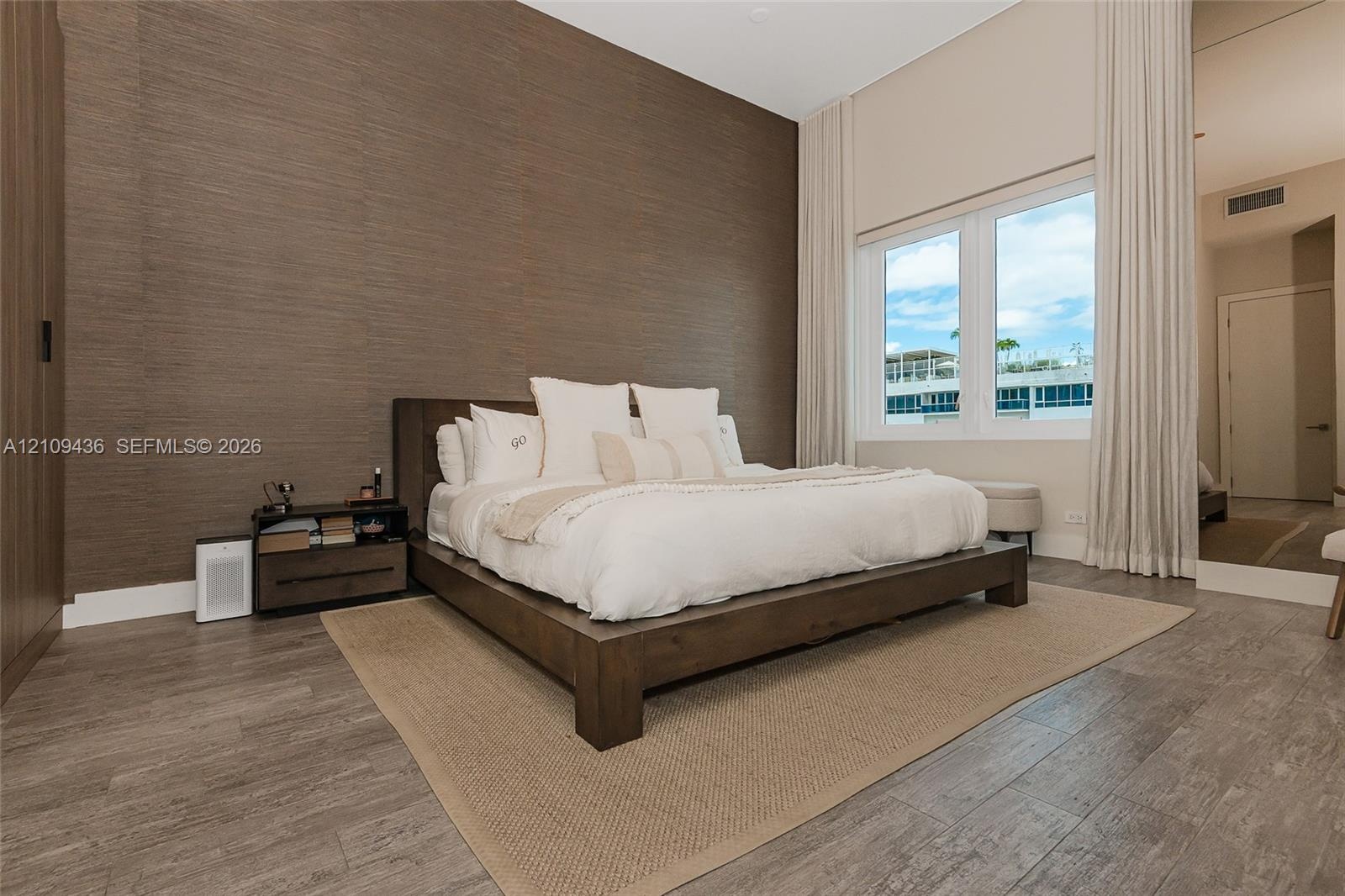 Textured accent wall, wood-finish flooring, vaulted ceiling, and full-length window treatments