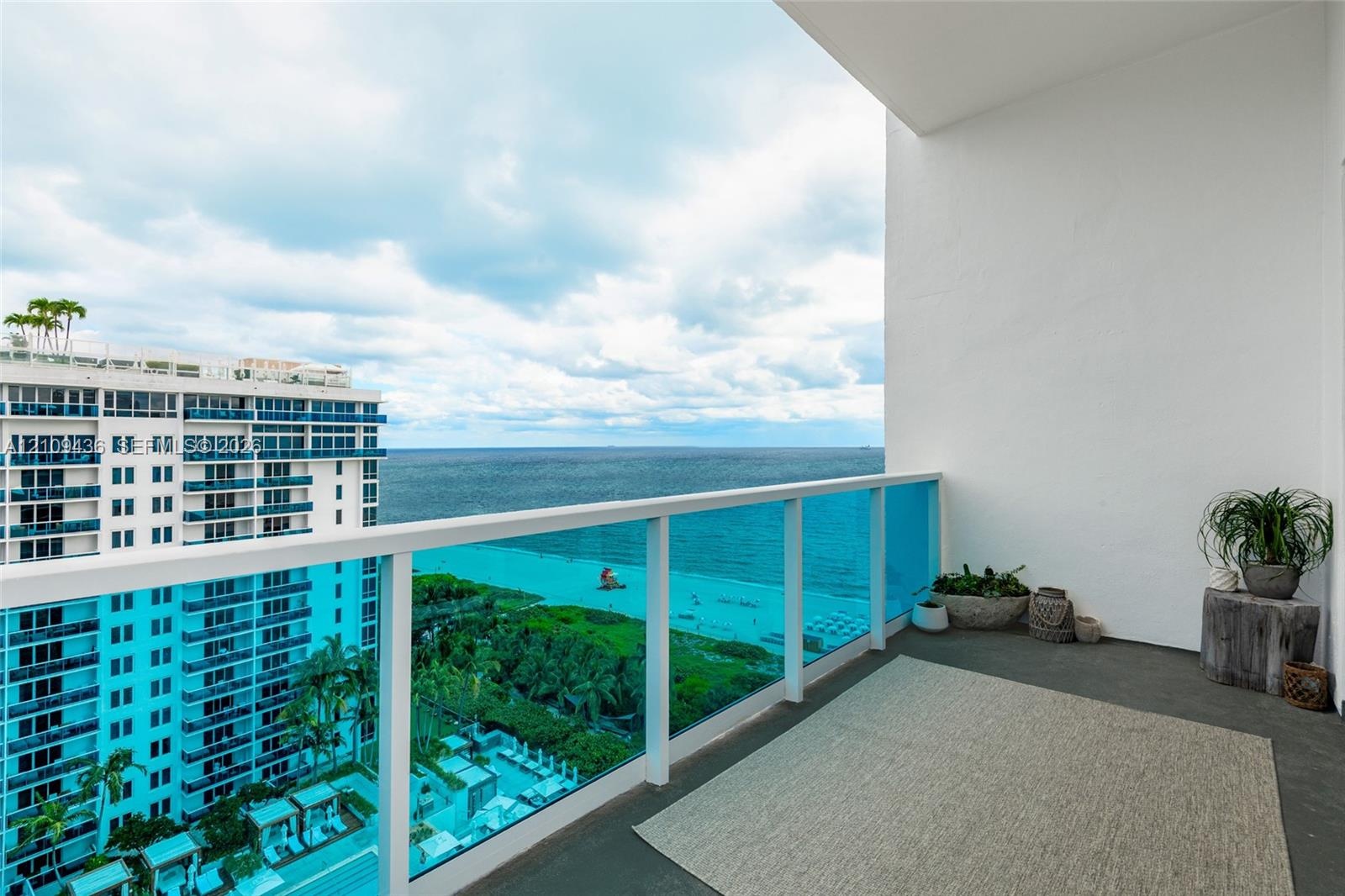 Private balcony featuring a glass-panel railing and concrete flooring, showcasing an expansive ocean and coastal panorama