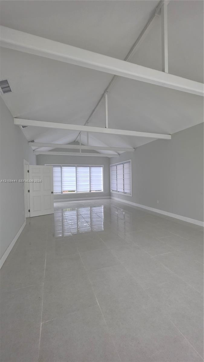 Vaulted ceiling with exposed white beams, large-format tile flooring, and multiple windows with horizontal blinds