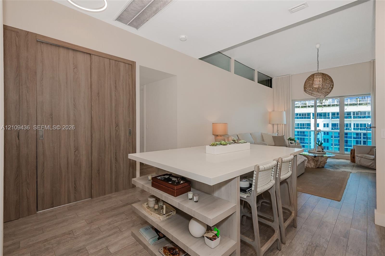 Central island with integrated shelving and solid surface countertop, wood-finish flooring, floor-to-ceiling wood-finish sliding doors, and clerestory