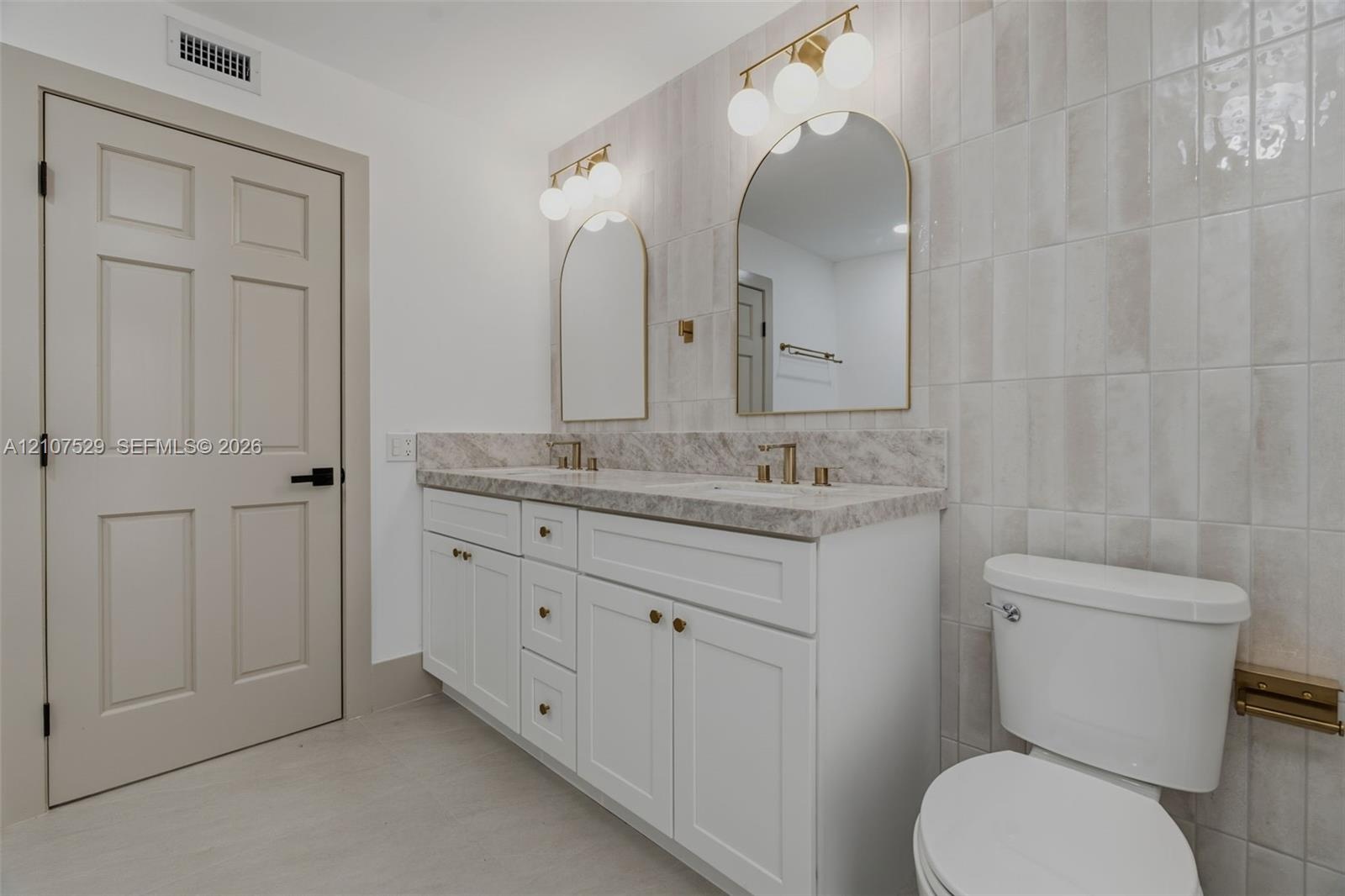 Double vanity featuring white cabinetry, stone-patterned countertop, arched mirrors, metallic hardware, and floor-to-ceiling cabinetry