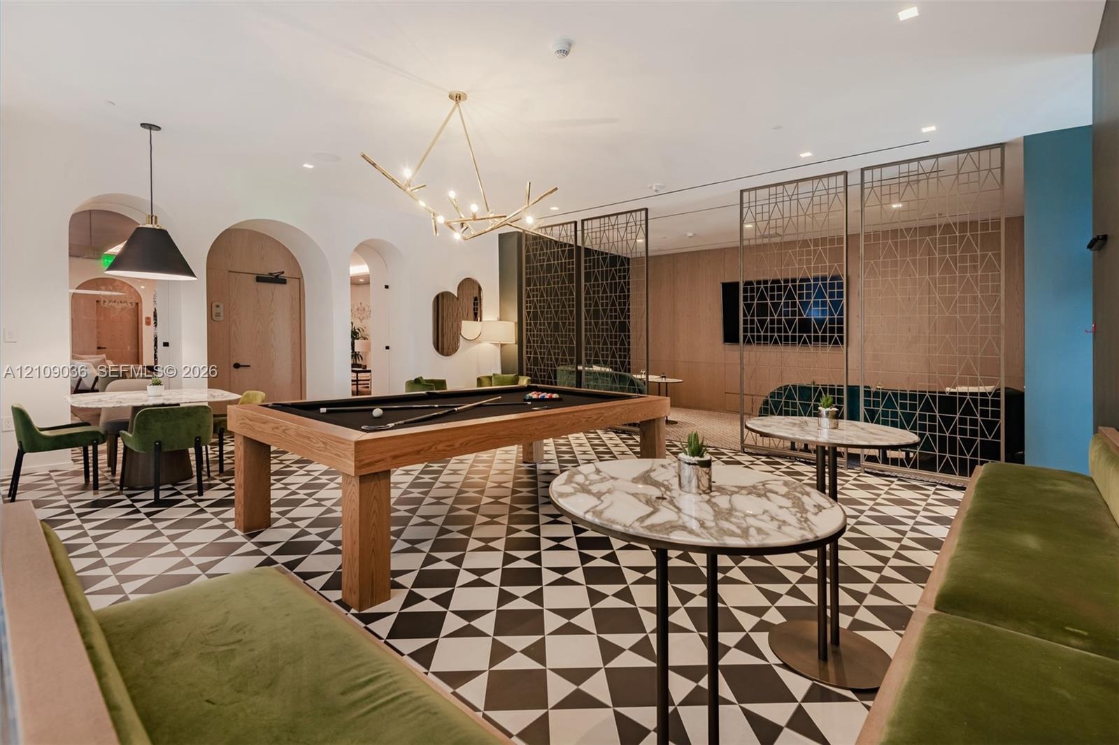 Geometric patterned tile flooring, arched wall openings, decorative metal privacy screens, wood-paneled accent wall, and multi-arm chandelier
