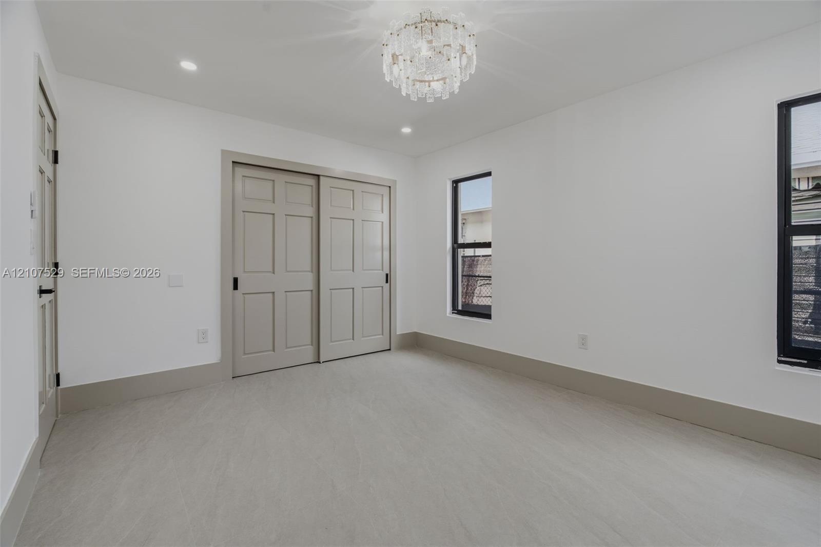 Neutral interior featuring large-format tile flooring, drum-style ceiling light fixture, recessed lighting, and windows with black frames