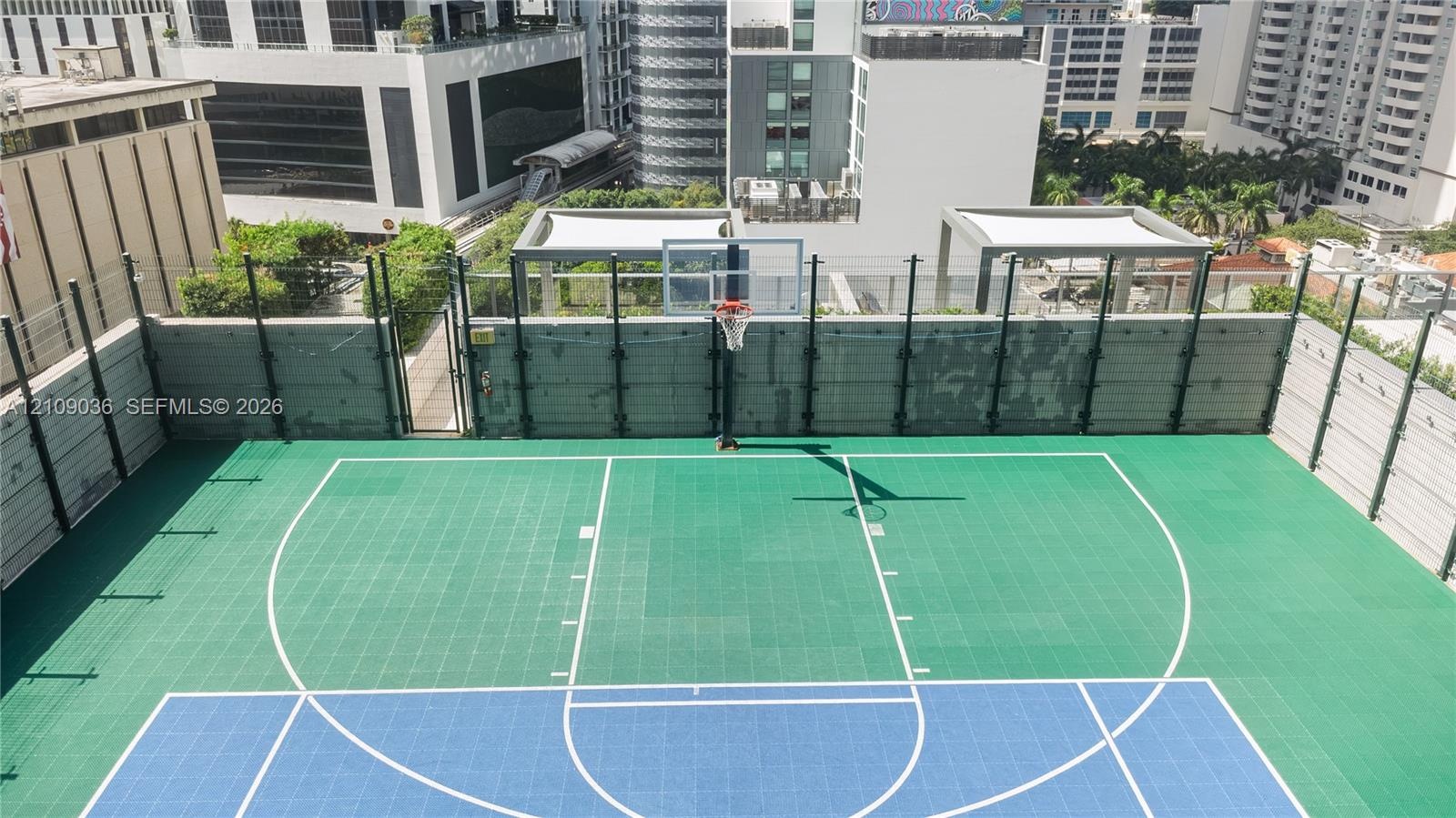 Rooftop basketball court featuring a multi-colored modular athletic surface, regulation-style hoop with glass backboard, and protective perimeter fenc