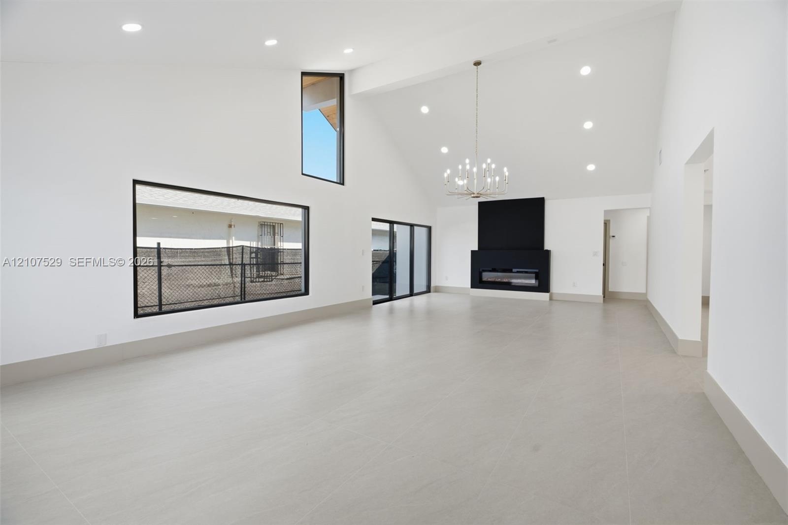 Kitchen featuring shaker-style cabinetry, an expansive center island with stone-finish countertops, matte black appliances, modern multi-globe chandel