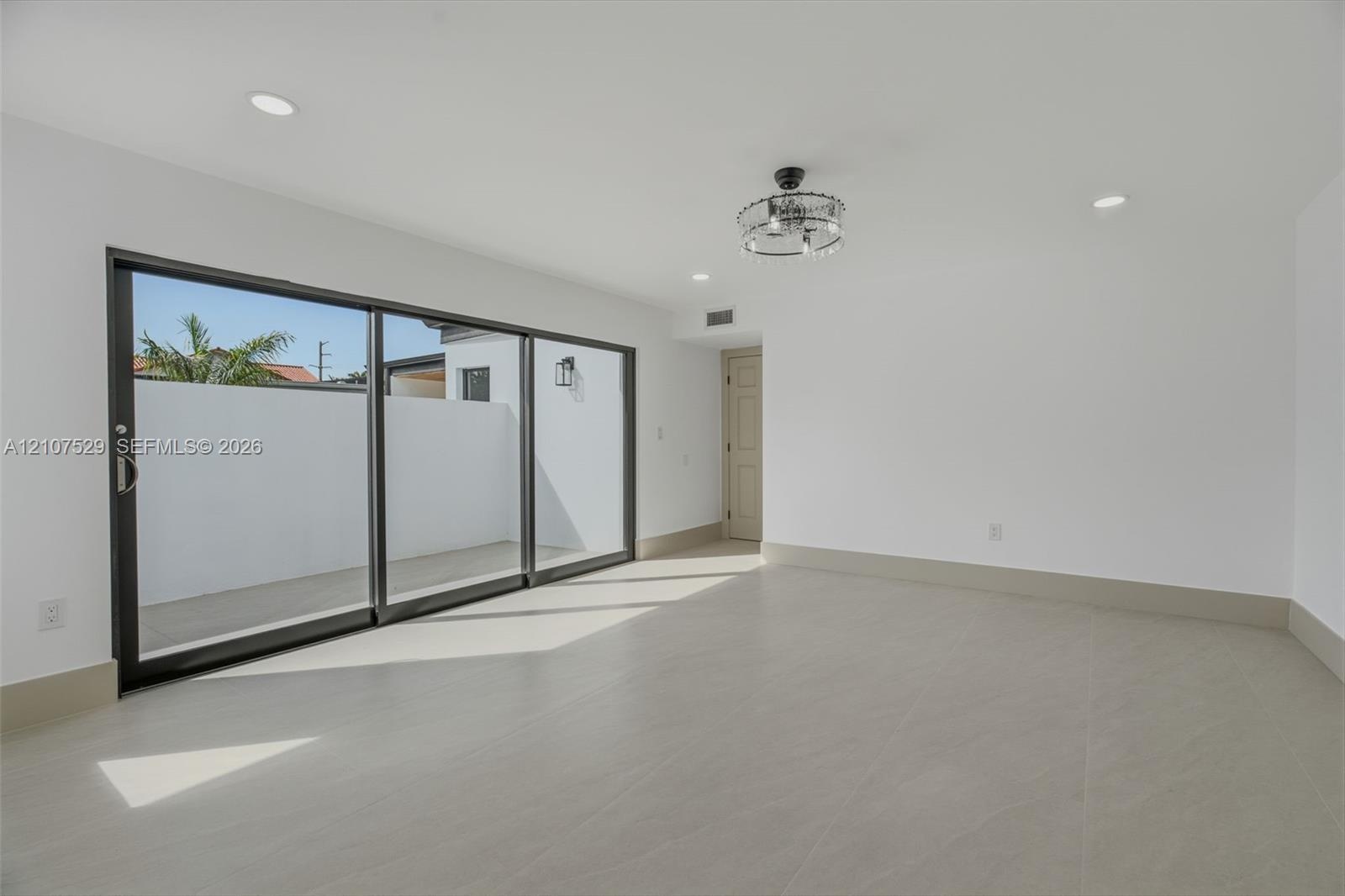 Spacious interior featuring large-format tile flooring, recessed lighting, a modern drum-style flush mount ceiling fixture, and black-trimmed windows